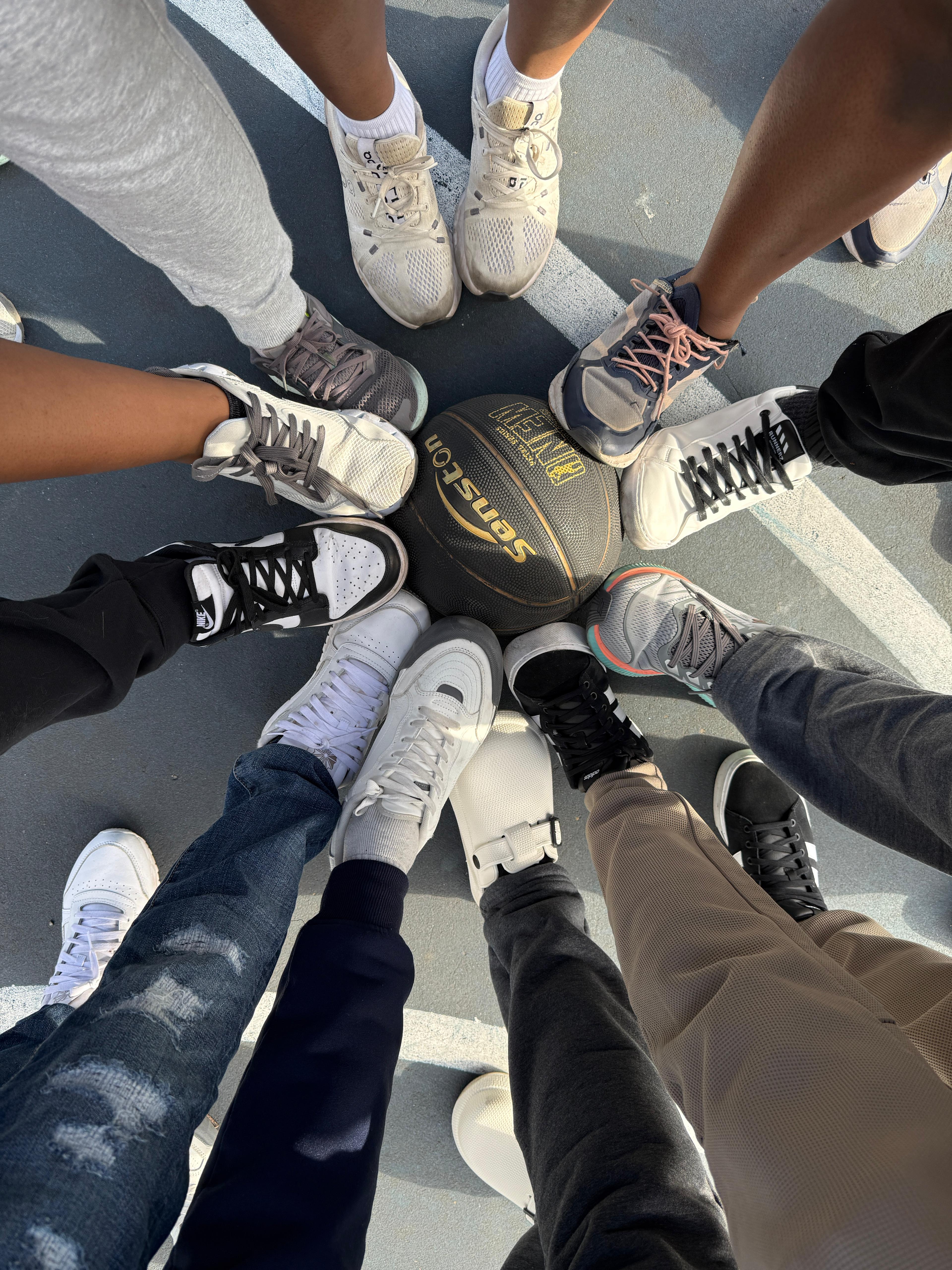MAGIS members placing their feet together around a basketball in a circle