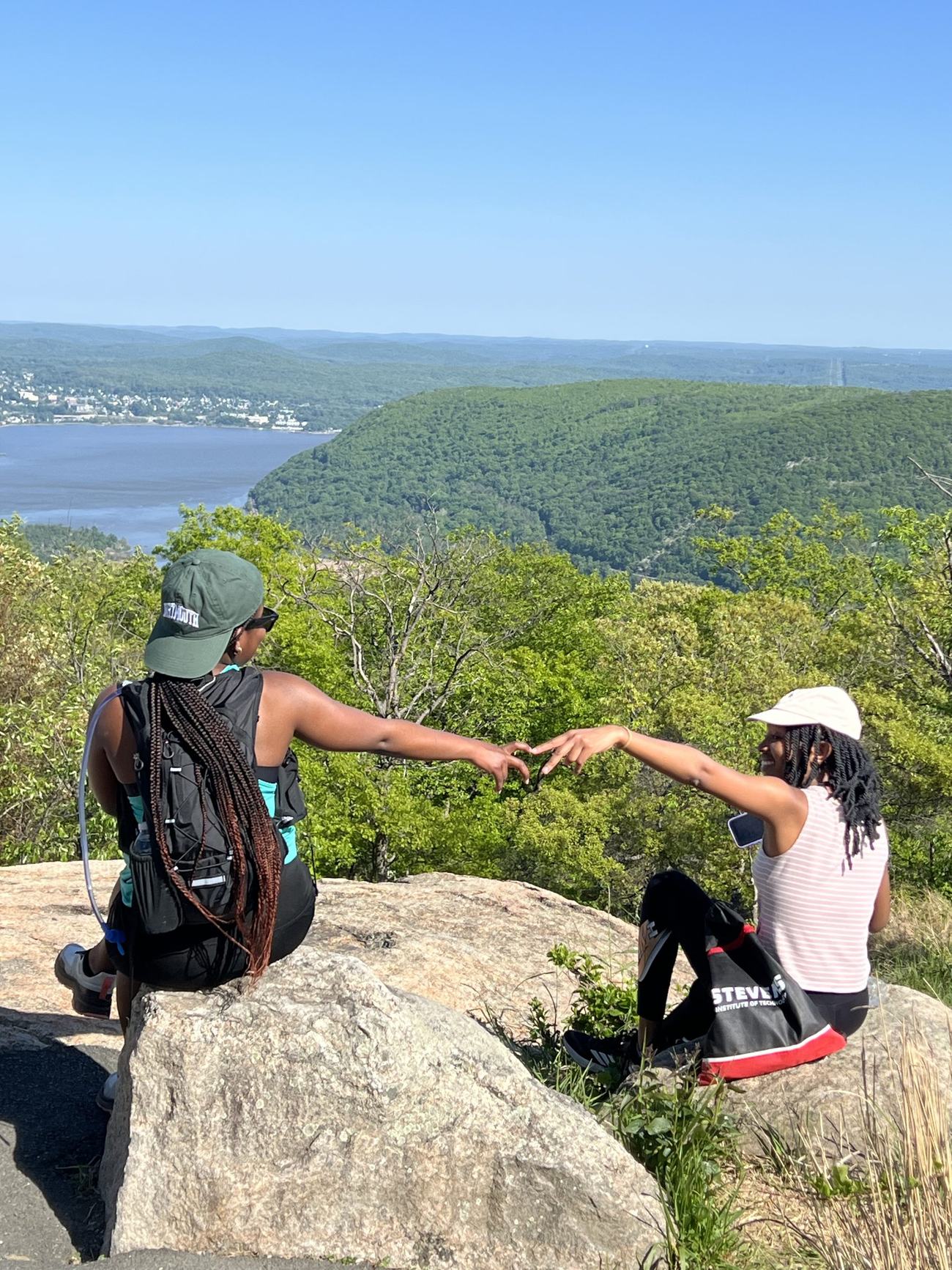 Two MAGIS hikers making a heart with their hands above a river valley